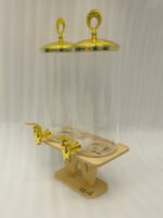 Two tall clear glass drink dispensers with gold spigots and circular gold finial lids resting on a wooden W-shaped stand.
