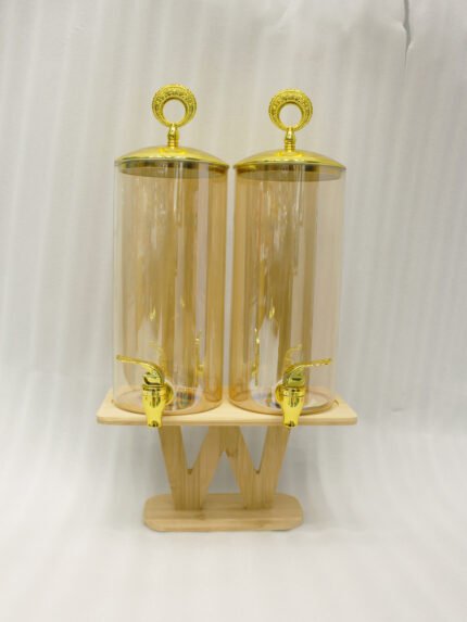 Dual 3.3L amber shaded glass beverage dispensers with gold lids and spigots on a W-shaped wooden stand sitting on a modern kitchen counter.