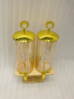 Dual 3.3L amber shaded glass beverage dispensers with gold lids and spigots on a W-shaped wooden stand sitting on a modern kitchen counter.