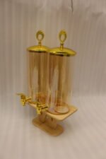 Dual 3.3L amber shaded glass beverage dispensers with gold lids and spigots on a W-shaped wooden stand sitting on a modern kitchen counter.