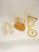 Elegant pink acrylic beverage dispenser with gold swan finial, gold spigot, stand, and 6 matching diamond-cut glasses.