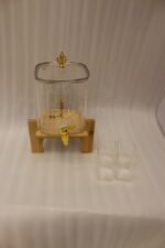 4.2L clear glass beverage dispenser with a gold spigot, gold lid handle, natural wooden stand, and 4 drinking glasses on a kitchen island.