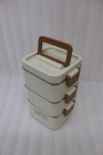 Cream and brown 3-tier stackable stainless steel lunch box with carrying handle on a kitchen counter