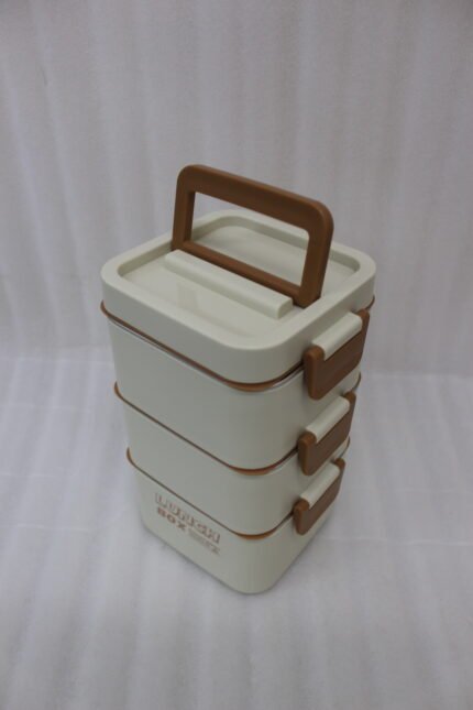 Cream and brown 3-tier stackable stainless steel lunch box with carrying handle on a kitchen counter