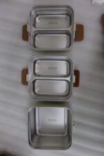 Cream and brown 3-tier stackable stainless steel lunch box with carrying handle on a kitchen counter