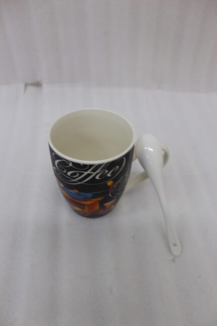 Black ceramic coffee mug printed with vintage grinder graphic and a white spoon resting in the handle slot on a granite kitchen counter.