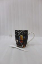 Black ceramic mug printed with vintage Coffee artwork resting on a granite kitchen counter alongside a white ceramic spoon.