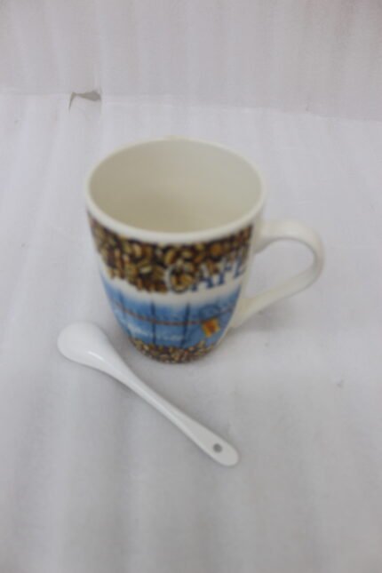 Tall ceramic mug with coffee bean print, blue cafe design, and matching ceramic spoon sitting on a kitchen marble countertop.