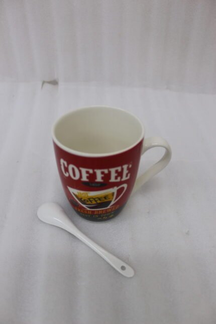 Red printed ceramic coffee mug featuring retro coffee shop logo next to a small white spoon on a kitchen counter