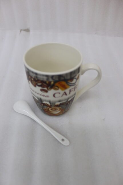 White ceramic mug printed with vintage cafe design, roasted coffee beans, cappuccino latte art, and a white ceramic spoon on a kitchen counter.