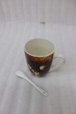Ceramic mug featuring a full-wrap printed coffee bean and espresso graphic sitting on a kitchen counter next to a matching white ceramic spoon.