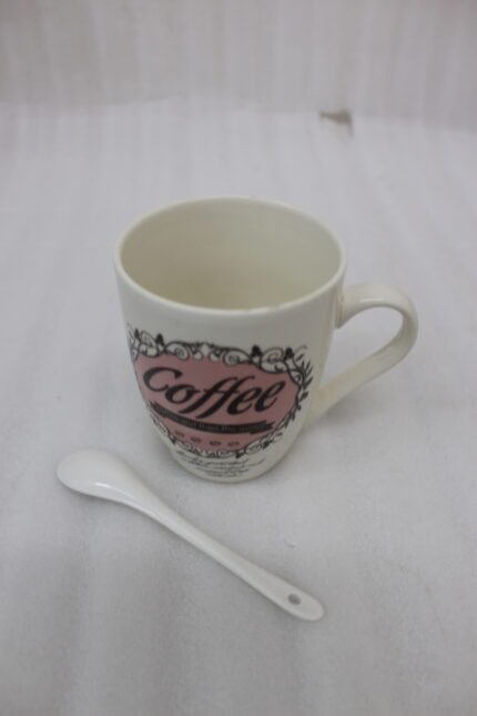 Vintage off-white ceramic coffee mug with "Coffee and then the world" text design resting on a grey countertop next to a white ceramic spoon.