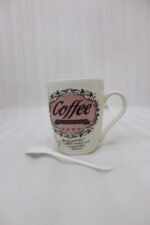 Vintage off-white ceramic coffee mug with "Coffee and then the world" text design resting on a grey countertop next to a white ceramic spoon.