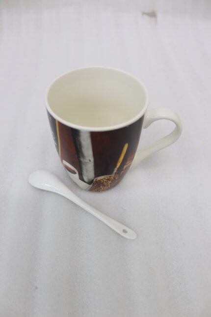 Printed ceramic coffee mug featuring coffee beans and cups artwork next to a small white ceramic spoon on a granite countertop