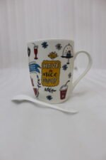 White ceramic coffee mug printed with 'Have a Nice Day' doodle art next to a matching ceramic spoon on a kitchen counter.