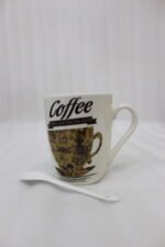 White ceramic coffee mug printed with 'Coffee and then the world' text and vintage coffee art next to a white spoon on a kitchen counter.
