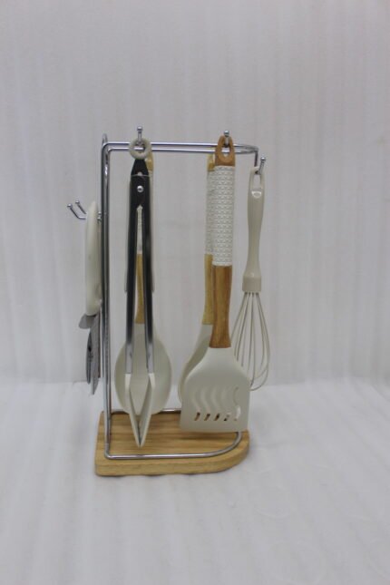8 piece white silicone kitchen utensil set hanging on a stainless steel stand with wooden handles on a wooden countertop