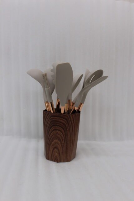 11-piece cream silicone kitchen utensil set with rose gold handles in a wooden holder on a marble countertop