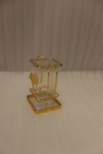 Luxury gold frame spoon stand with fluted clear acrylic container featuring a gold ginkgo leaf emblem on a marble countertop.