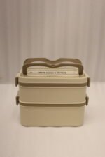 Beige and brown 2 in 1 double layer bento lunch box with locking latches on a kitchen counter