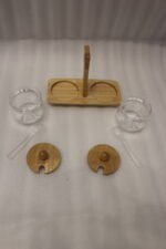 Two clear acrylic condiment jars with wooden lids and glass spoons set on a wooden stand tray with handle on a white marble countertop.