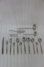 72-piece polished stainless steel cutlery set arranged on a cloth napkin featuring place settings, ladles, cake server, and tongs.