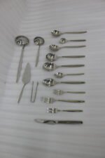 72-piece polished stainless steel cutlery set arranged on a cloth napkin featuring place settings, ladles, cake server, and tongs.