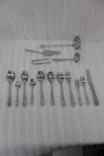 A Diverse Arrangement of Polished Silver-Toned Cutlery on a Textured Linen Mat, Featuring 12-Person Service and Loose Ladles, a Cake Server, and Tongs in the Background.