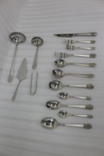 A Diverse Arrangement of Polished Silver-Toned Cutlery on a Textured Linen Mat, Featuring 12-Person Service and Loose Ladles, a Cake Server, and Tongs in the Background.