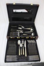 72-piece stainless steel cutlery and serving set with dual-tone gold textured handles laid out on a linen cloth.