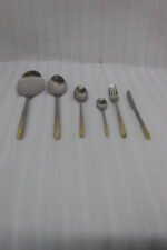 Stainless steel cutlery set with textured gold handles and floral engravings displayed on a beige cloth.