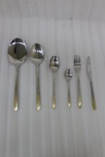 Stainless steel cutlery set with textured gold handles and floral engravings displayed on a beige cloth.