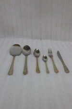 Gold-embossed stainless steel cutlery set including spoons, fork, and knife arranged on a beige cloth table setting.
