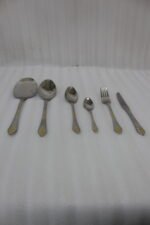 Six-piece luxury stainless steel cutlery set featuring textured handles with gold filigree details displayed on a beige linen napkin.