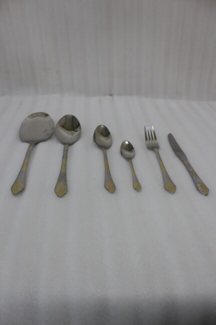 Six-piece luxury stainless steel cutlery set featuring textured handles with gold filigree details displayed on a beige linen napkin.