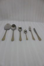 Stainless steel cutlery set with gold patterned handles featuring serving spoons, dinner forks, knives, and dessert spoons on a linen cloth.