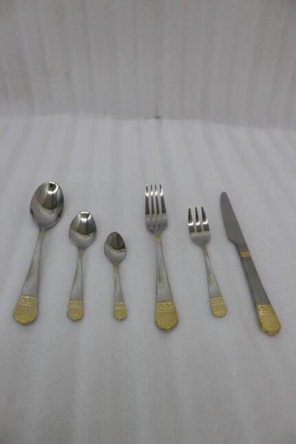 36-piece polished stainless steel cutlery set with ornate gold-accented handles arranged on a linen napkin.