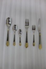 36-piece polished stainless steel cutlery set with ornate gold-accented handles arranged on a linen napkin.
