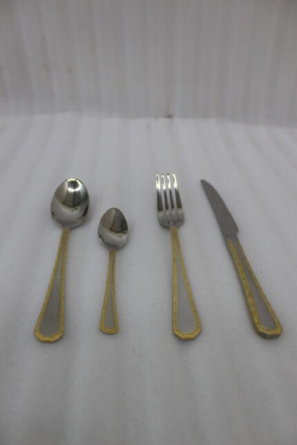 24-piece stainless steel cutlery set with gold-bordered handles including a rice spoon, sweet spoon, fork, and knife arranged on a grey placemat.
