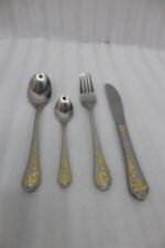 24 piece mirror polish stainless steel cutlery set with ornate gold heart handle detailing on a folded napkin