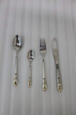 24-piece stainless steel cutlery set featuring gold "Love" engravings on handles, including rice spoon, sweet spoon, fork, and knife on a gray napkin.
