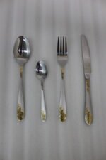 24-piece silver stainless steel cutlery set with gold floral embossed handles displayed on a linen napkin.