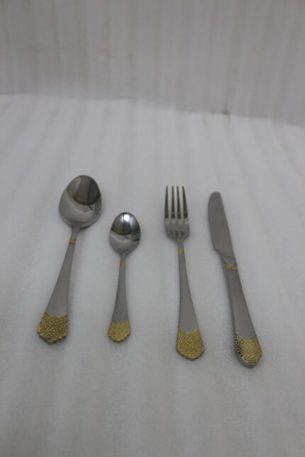 24-piece polished stainless steel cutlery set with gold filigree handle accents arranged on a beige cloth.