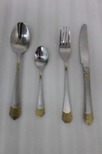 24-piece polished stainless steel cutlery set with gold filigree handle accents arranged on a beige cloth.