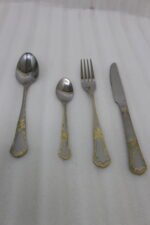 24-piece stainless steel cutlery set with ornate gold embossed handles laid out on a beige linen napkin