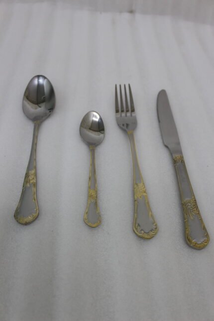 24-piece stainless steel cutlery set with ornate gold embossed handles laid out on a beige linen napkin