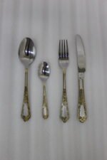 Luxury 24-piece stainless steel cutlery set with ornate gold embossed handles arranged on a linen napkin