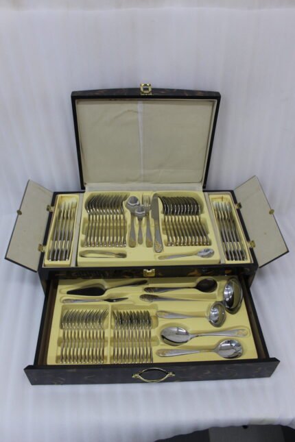 72-piece silver stainless steel cutlery set with embossed gold handles displayed on a linen mat.