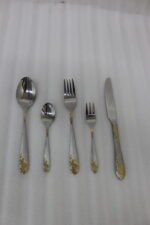 72-piece silver stainless steel cutlery set with embossed gold handles displayed on a linen mat.