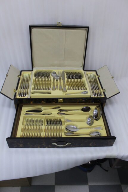 72-piece stainless steel cutlery set featuring embossed gold-plated handles laid out on a beige table runner.
